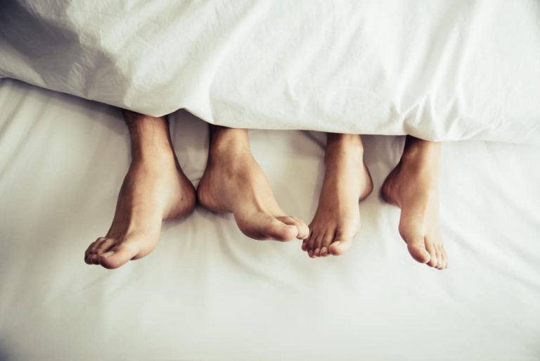 A couple's feet stick out from under white sheets after sex.