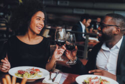 A black couple on a dinner date toasting with wine glasses