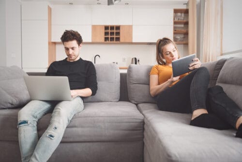 Disinterested couple sitting on a couch working on their computers. Expert advice if your relationship is in crisis.
