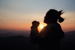 A woman prays on a mountain during sunset.