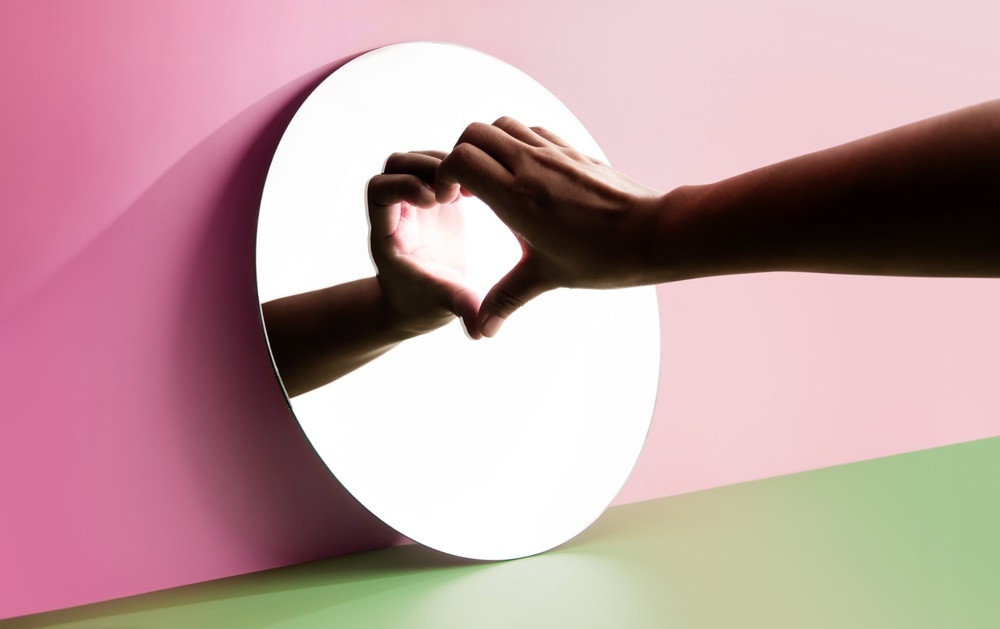 A makes the heart symbol in front of a mirror representing self love.