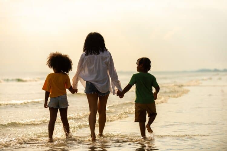 A single mom on vacation walks on the beach with her son and daughter at sunset.