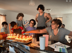 A woman living in a mommune lights the candles on a brithday cake.