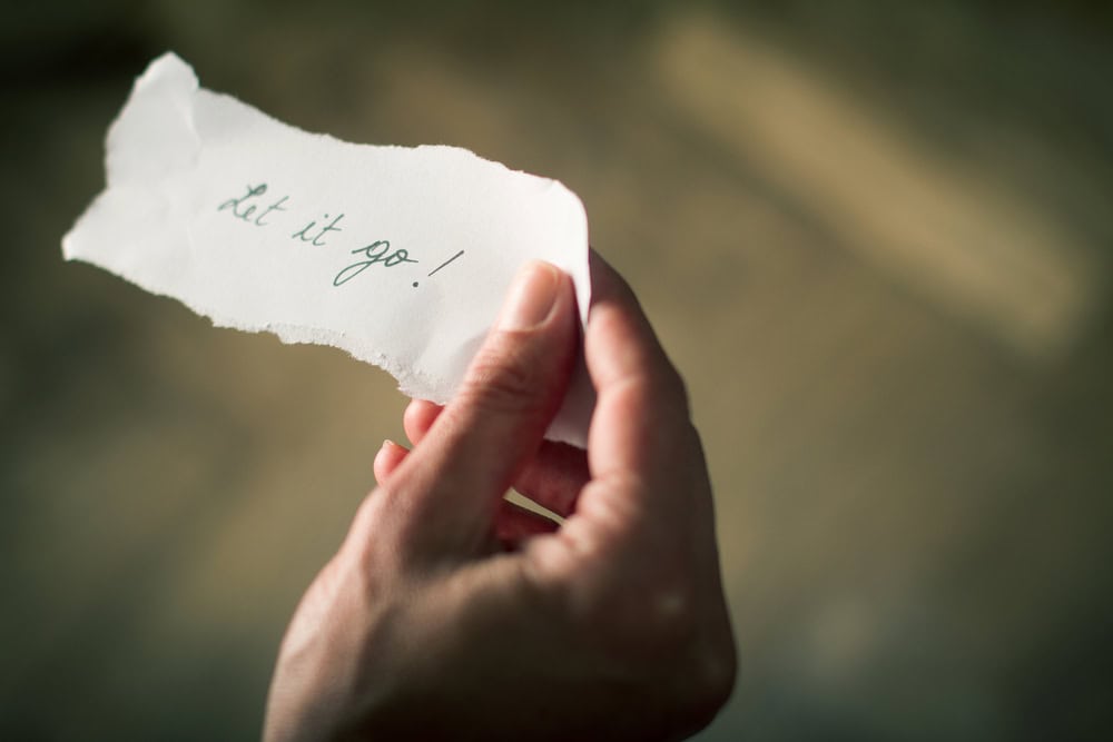 Hand holding a note of paper with the message let it go written on it