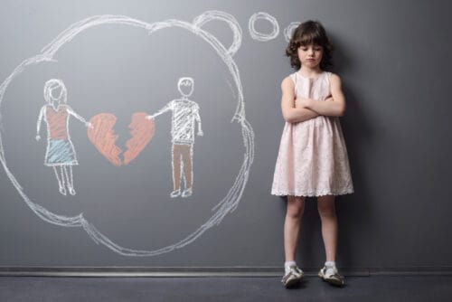 Little girl crossed her hands and looks very unhappy. Depicted divorce of the parents on the grey wall with chalk
