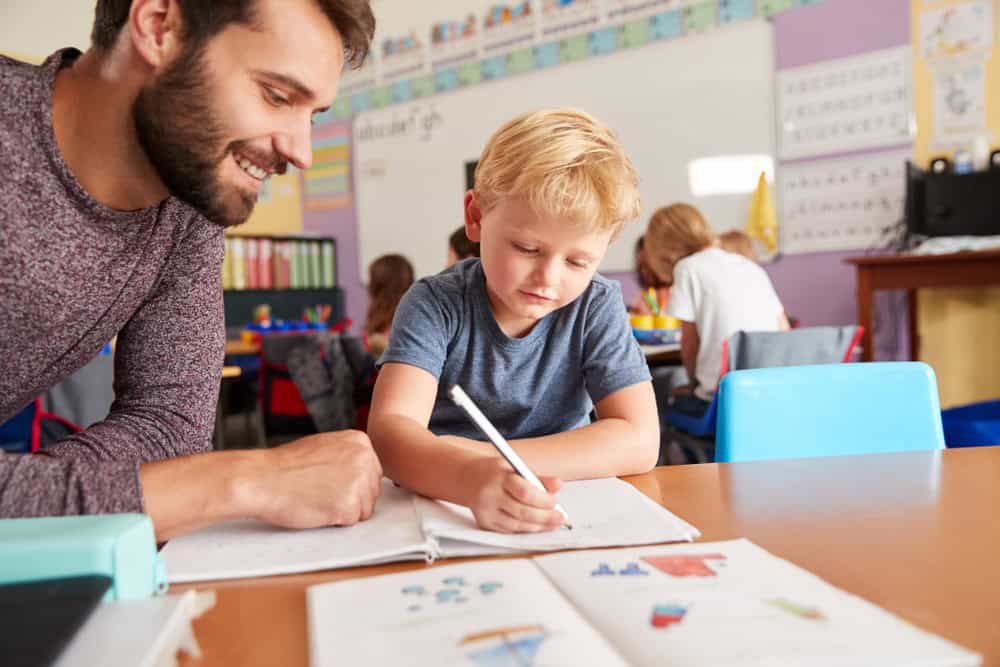 Elementary School Teacher Giving Male Pupil One To One Support In Classroom
