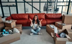 Young woman sitting in new house and raising arms in joy after moving in