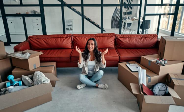 Young woman sitting in new house and raising arms in joy after moving in