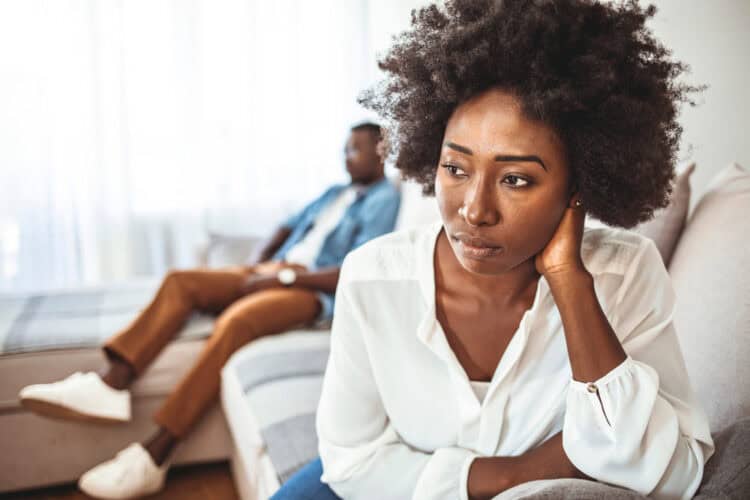 young girl thinking of relationships problems sitting on sofa with offended boyfriend, conflicts in marriage, upset couple after fight