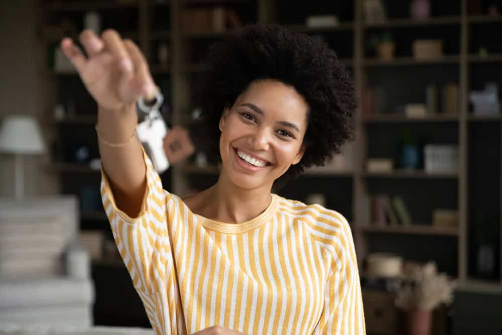 Happy joyful young African woman showing keys at camera. Just moved homeowner