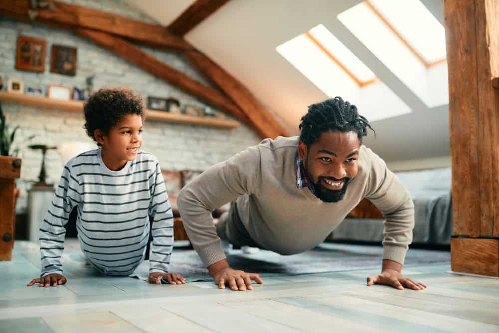 Happy role model and boy doing push-ups while working out together at home.